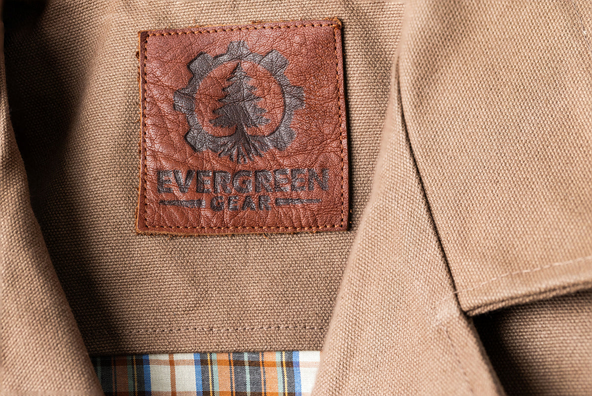 Close-up of a heavy canvas vest with a brown leather patch label reading EVERGREEN GEAR. USA Made